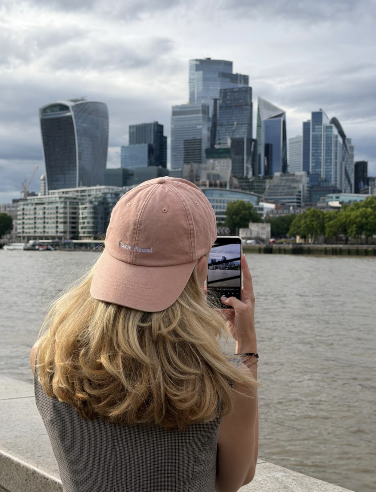 SJ photographing the City of London skyline from the Southbank, wearing the peach cap